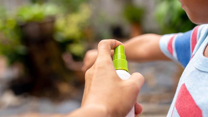 Father spraying insect repellents on his son arm in the garden