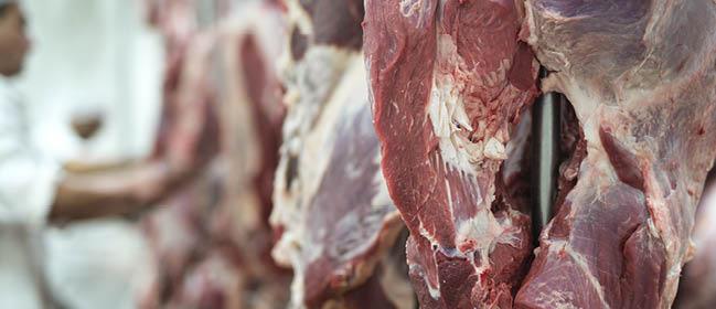 Fresh red meet and butchery worker working in background.