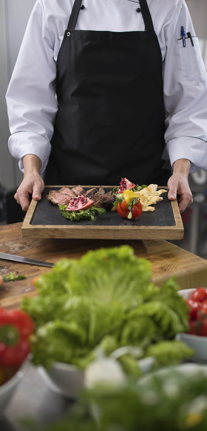 female Chef in hotel or restaurant kitchen holding grilled beef steak plate with vegetable decoration